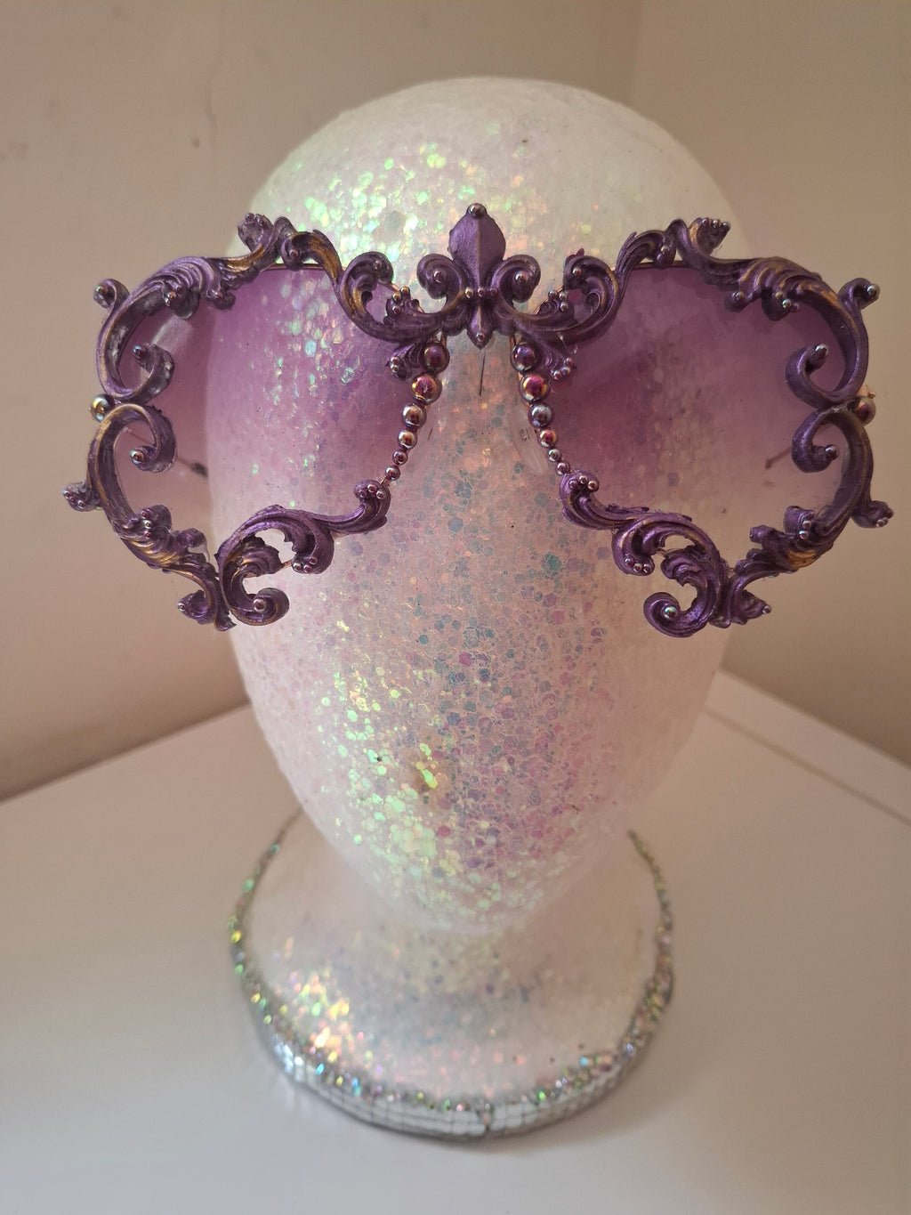 Hand-sculpted sunglasses in deep purple scrollwork with gold foil accents and a fleur-de-lis crown