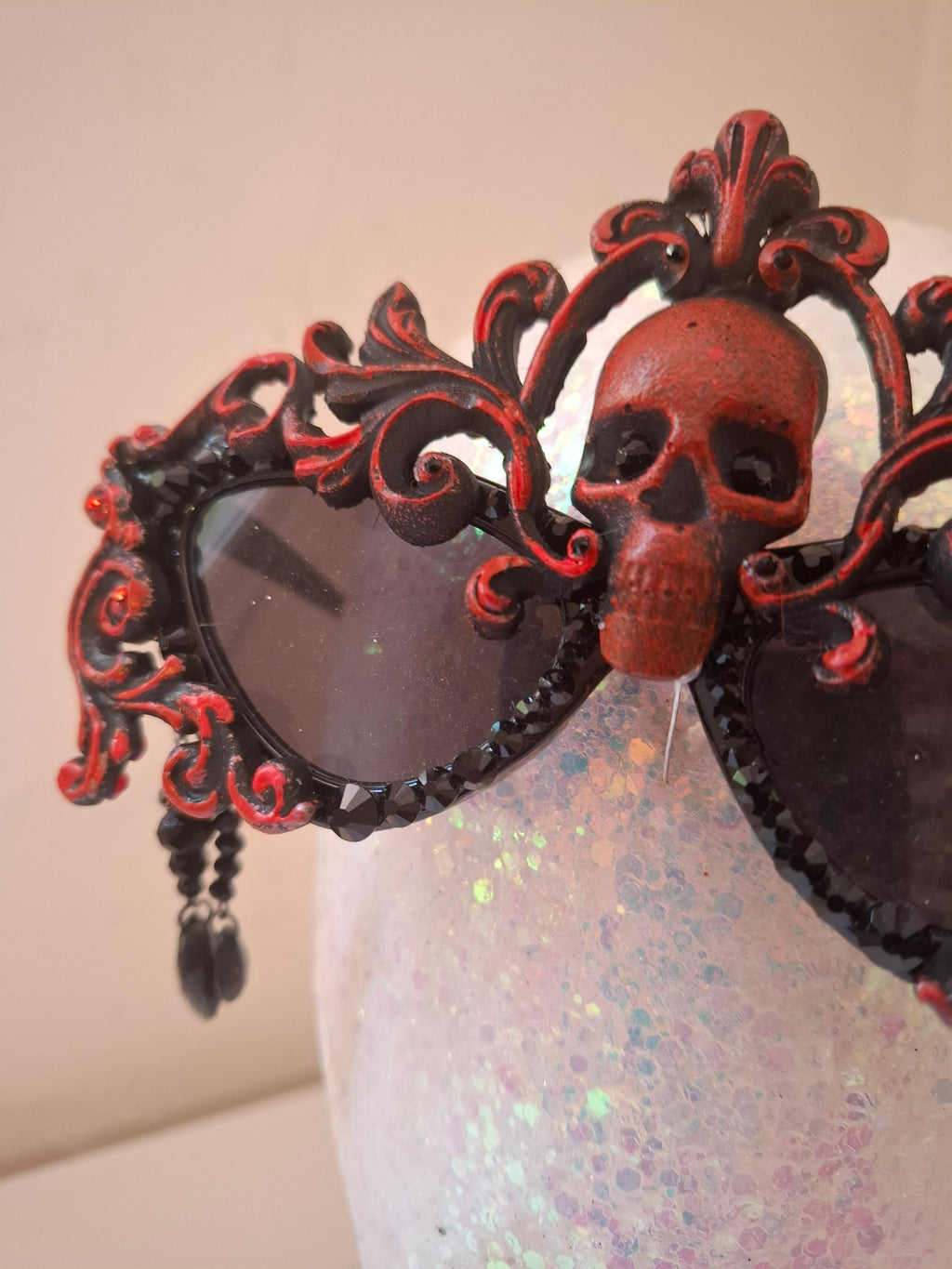 Hand-sculpted sunglasses in deep burgundy scrollwork with a skull centerpiece and black crystals
