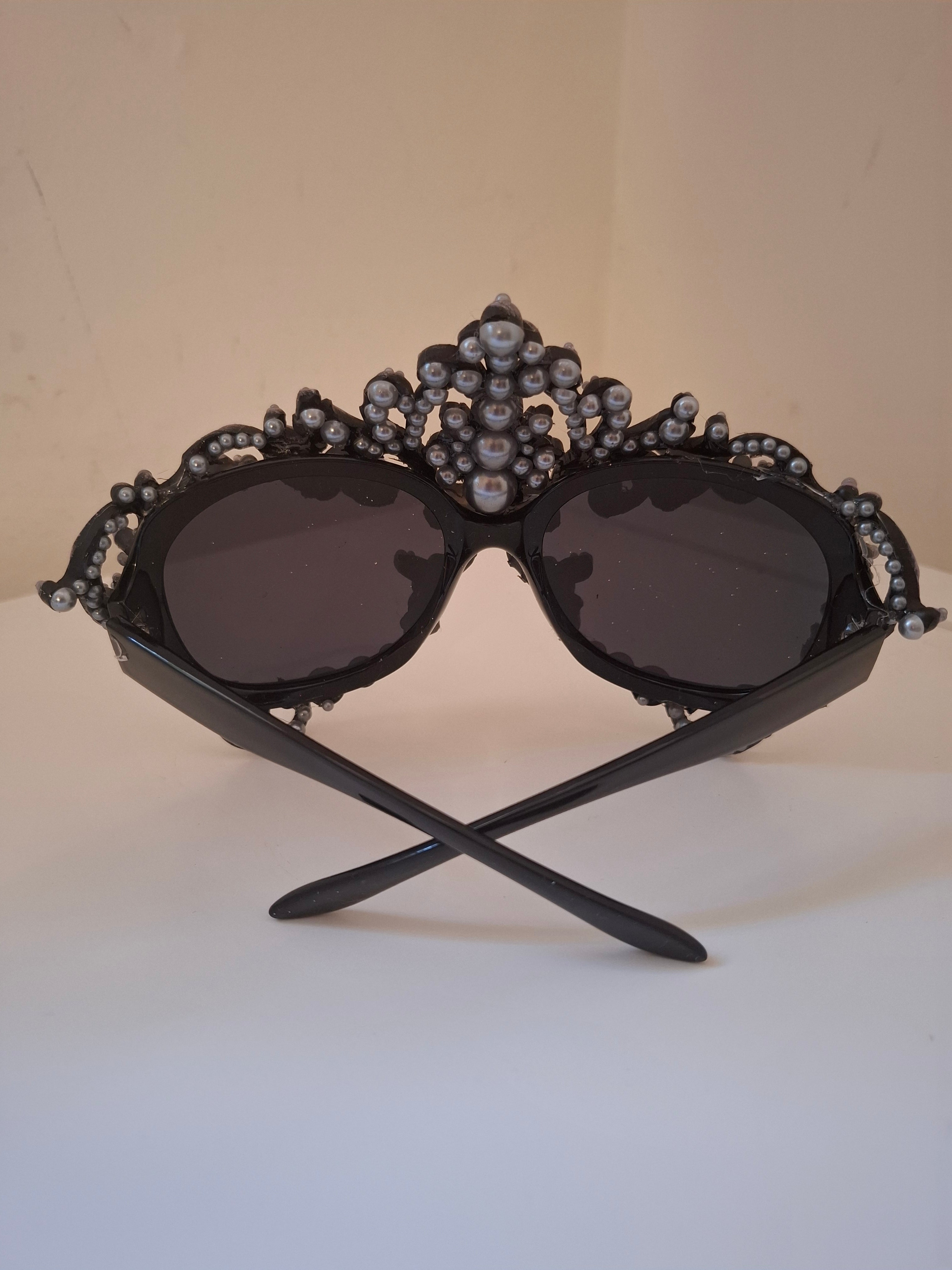  Hand-sculpted sunglasses in deep plum scrollwork with a fleur-de-lis crown and cascading pearl drops. 