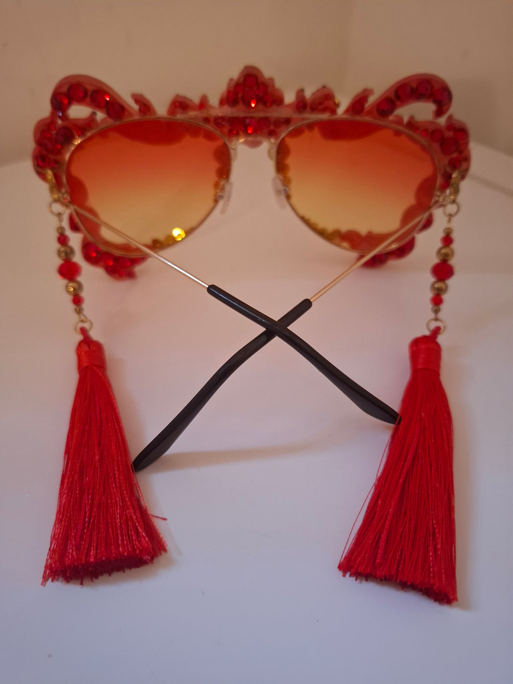 Hand-sculpted sunglasses in coral and gold flame scrollwork with crimson tassels. 