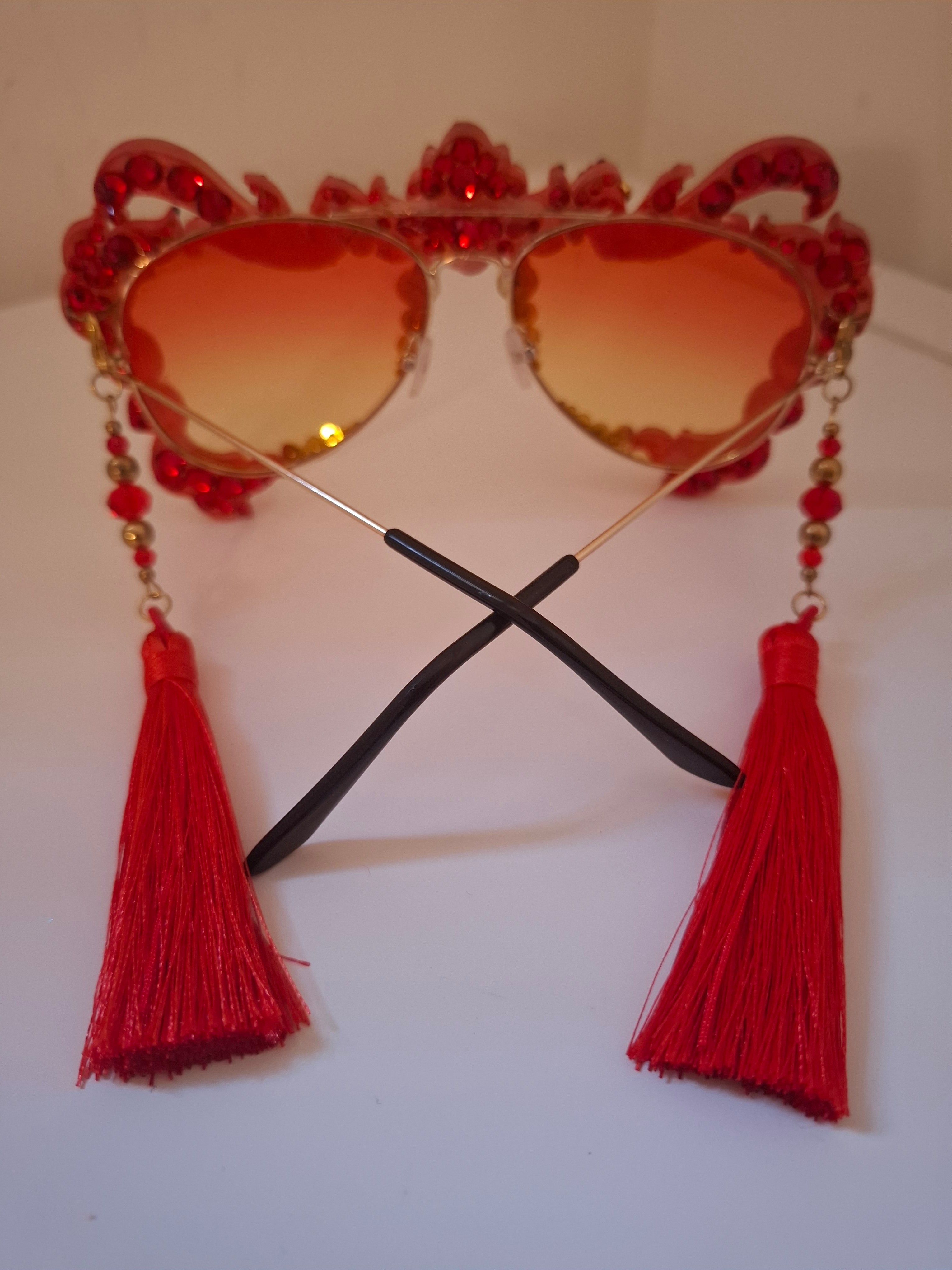 Hand-sculpted sunglasses in coral and gold flame scrollwork with crimson tassels. 