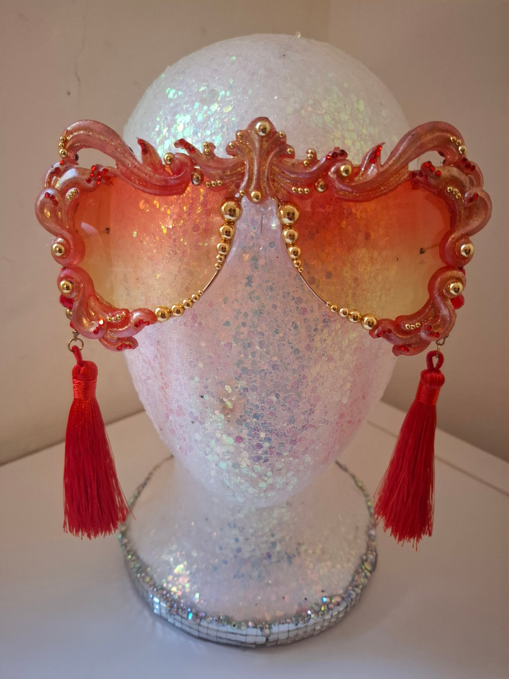 Hand-sculpted sunglasses in coral and gold flame scrollwork with crimson tassels. 