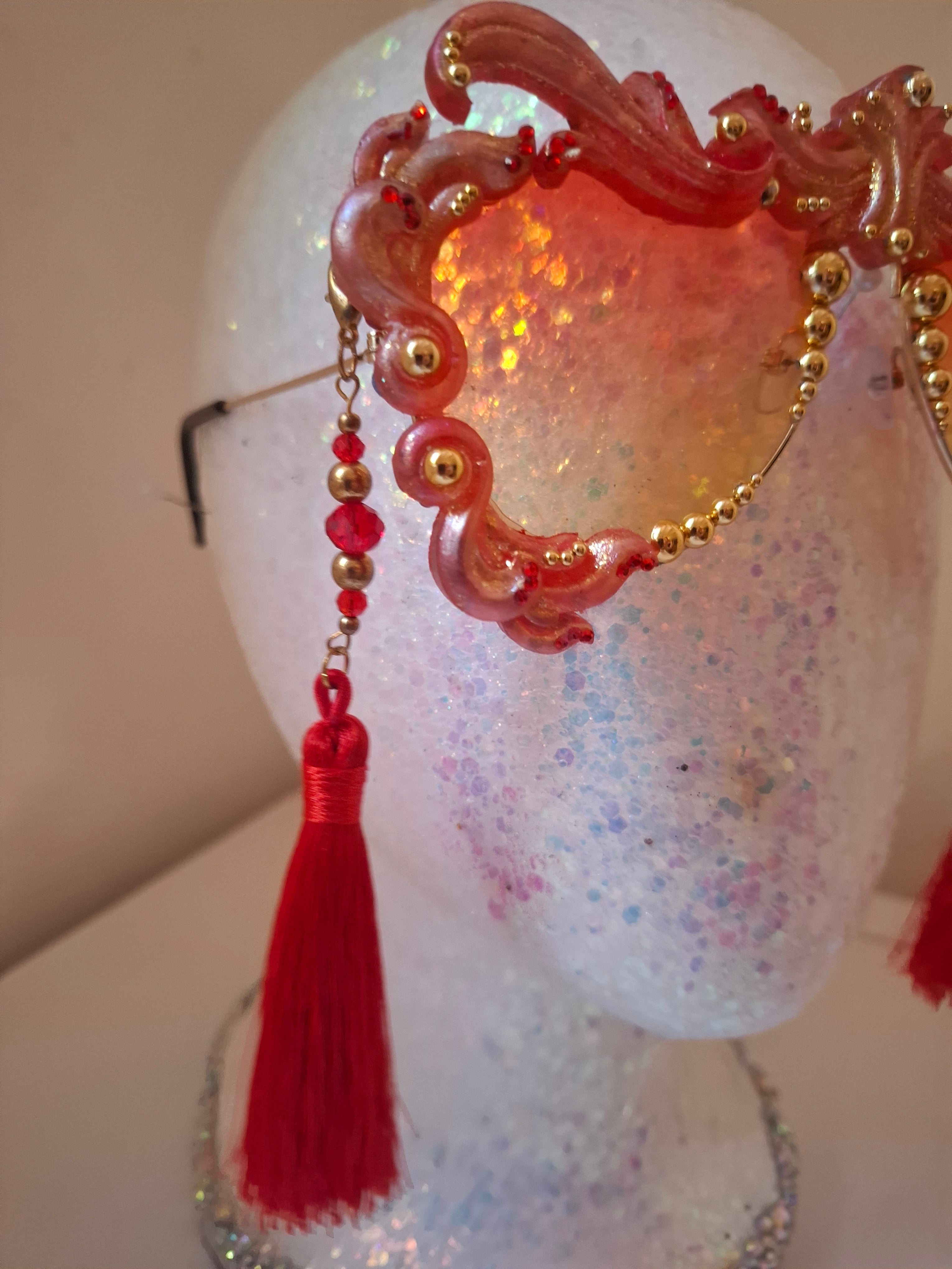 Hand-sculpted sunglasses in coral and gold flame scrollwork with crimson tassels. 