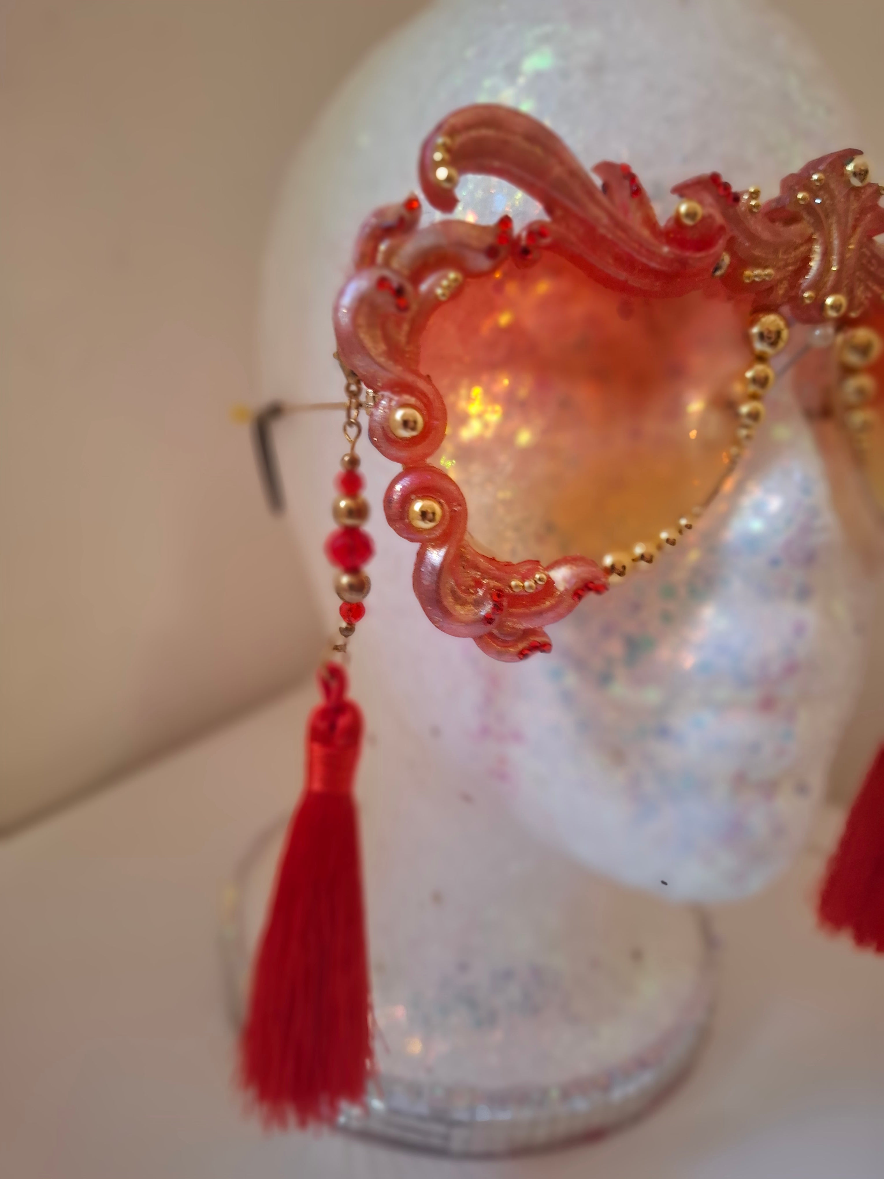 Hand-sculpted sunglasses in coral and gold flame scrollwork with crimson tassels. 