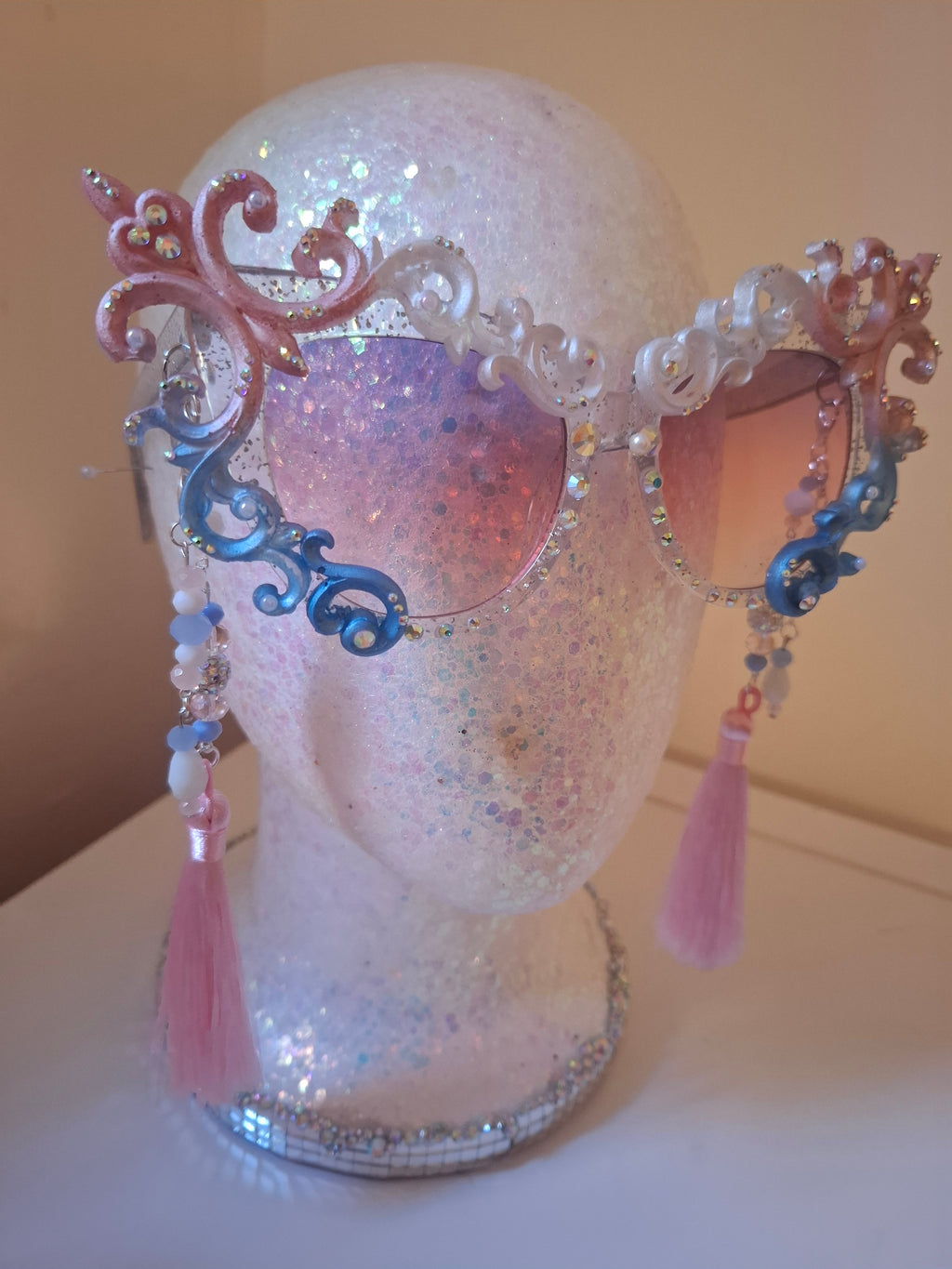 Hand-sculpted Pride sunglasses in trans flag colors — pink, white, and blue, with beaded tassels.

