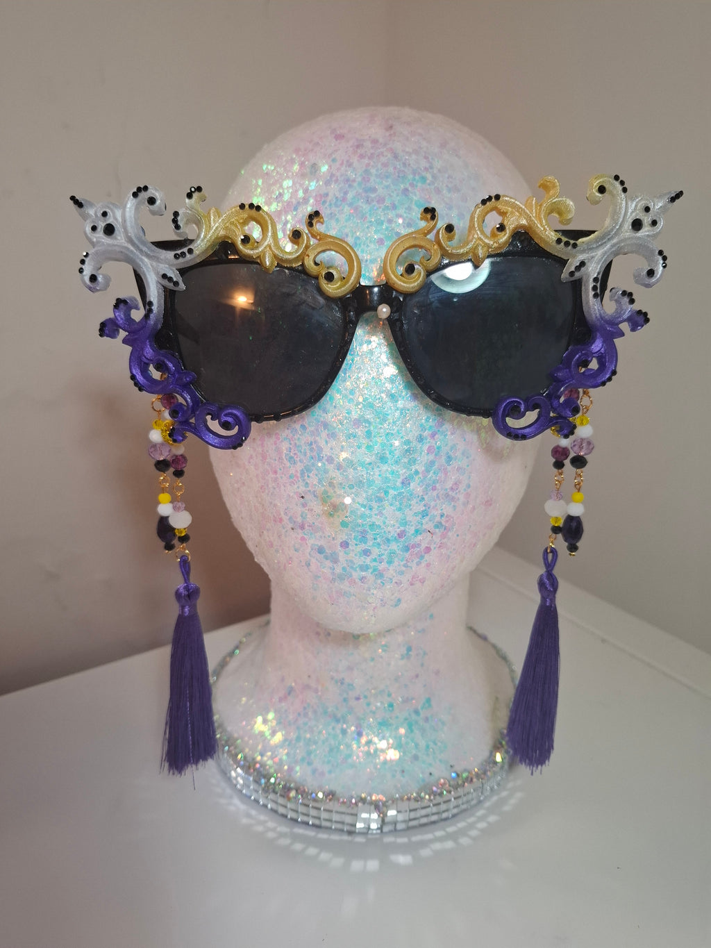 Hand-sculpted Pride sunglasses in non-binary flag colors — yellow, white, purple, and black, with beaded tassels.
