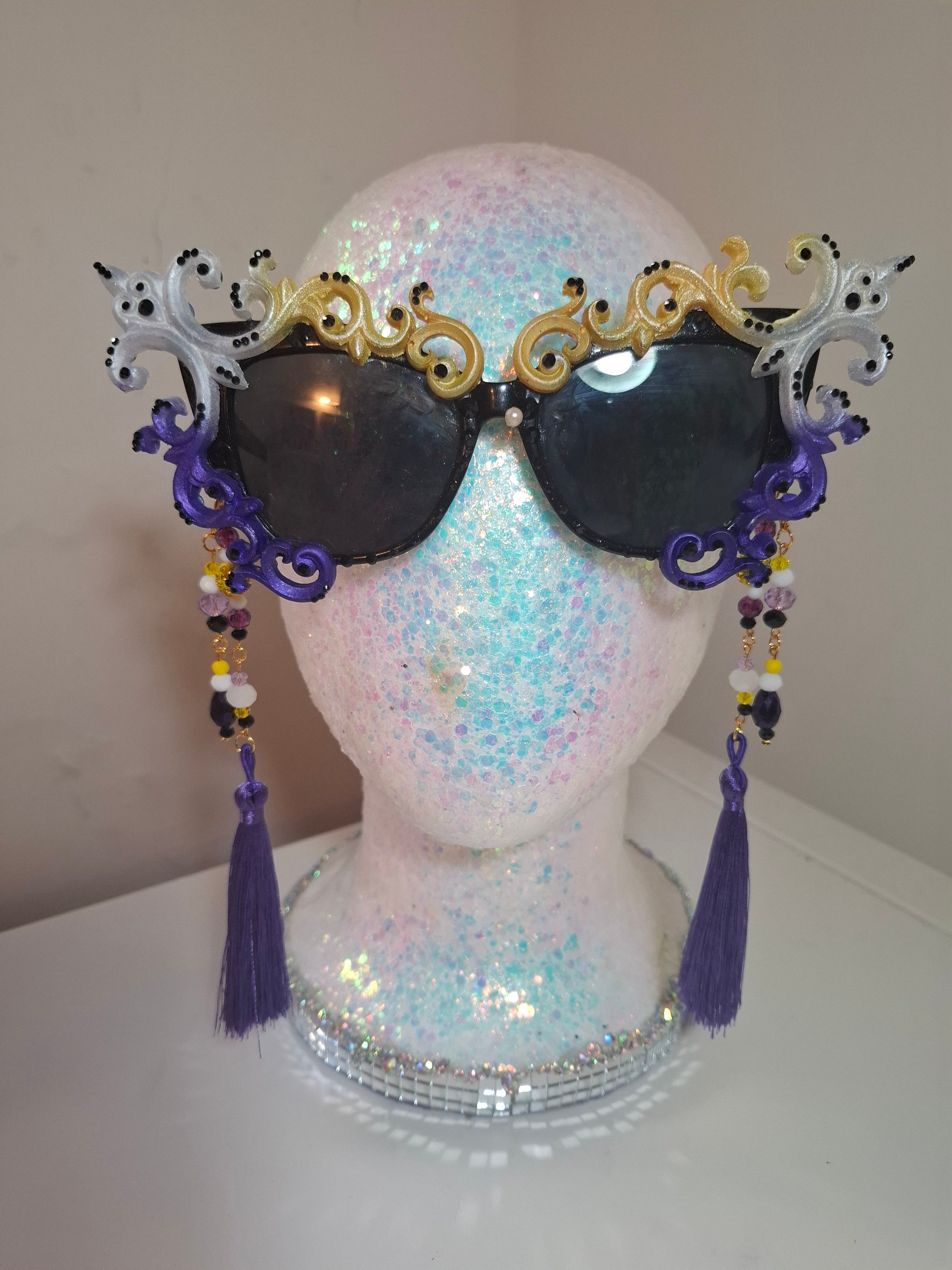 Hand-sculpted Pride sunglasses in non-binary flag colors — yellow, white, purple, and black, with beaded tassels.

