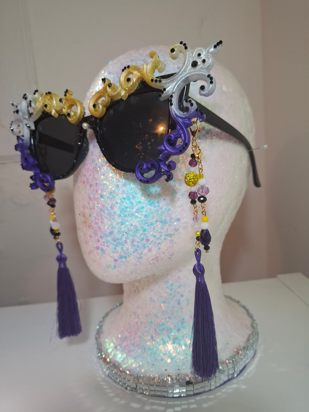 Hand-sculpted Pride sunglasses in non-binary flag colors — yellow, white, purple, and black, with beaded tassels.
