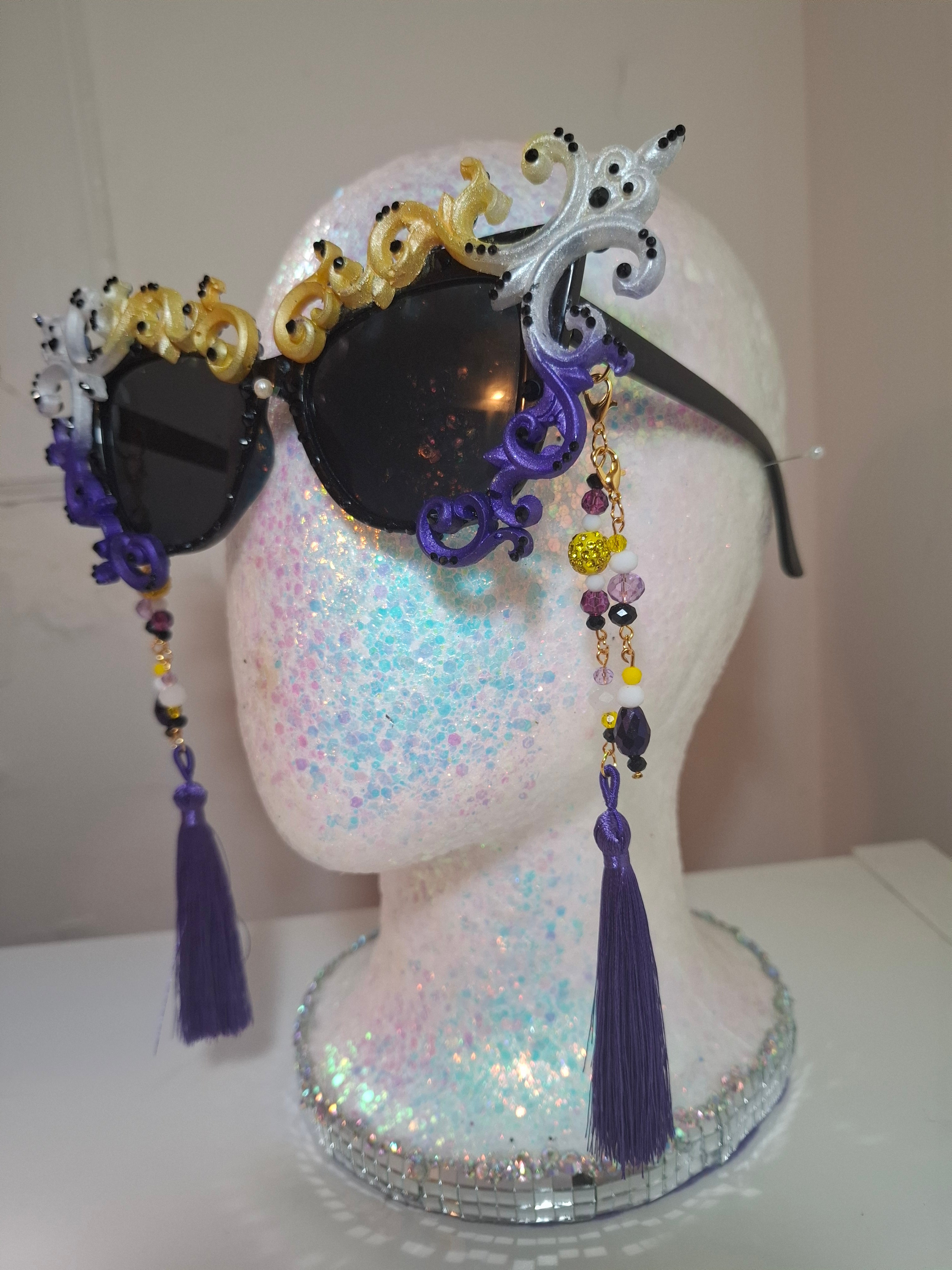 Hand-sculpted Pride sunglasses in non-binary flag colors — yellow, white, purple, and black, with beaded tassels.
