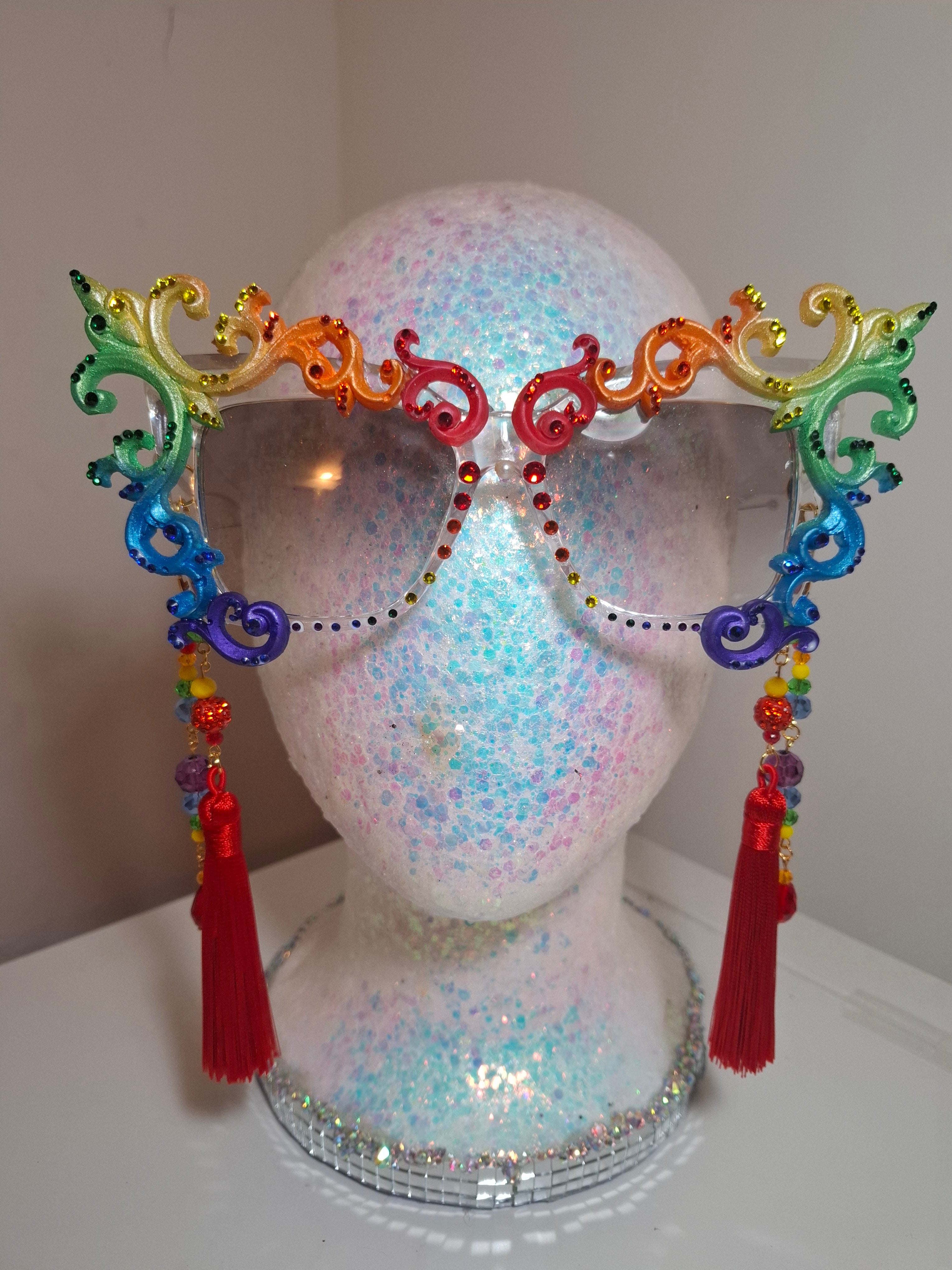 Hand-sculpted Pride sunglasses in classic rainbow flag colors, with red beaded tassels.
