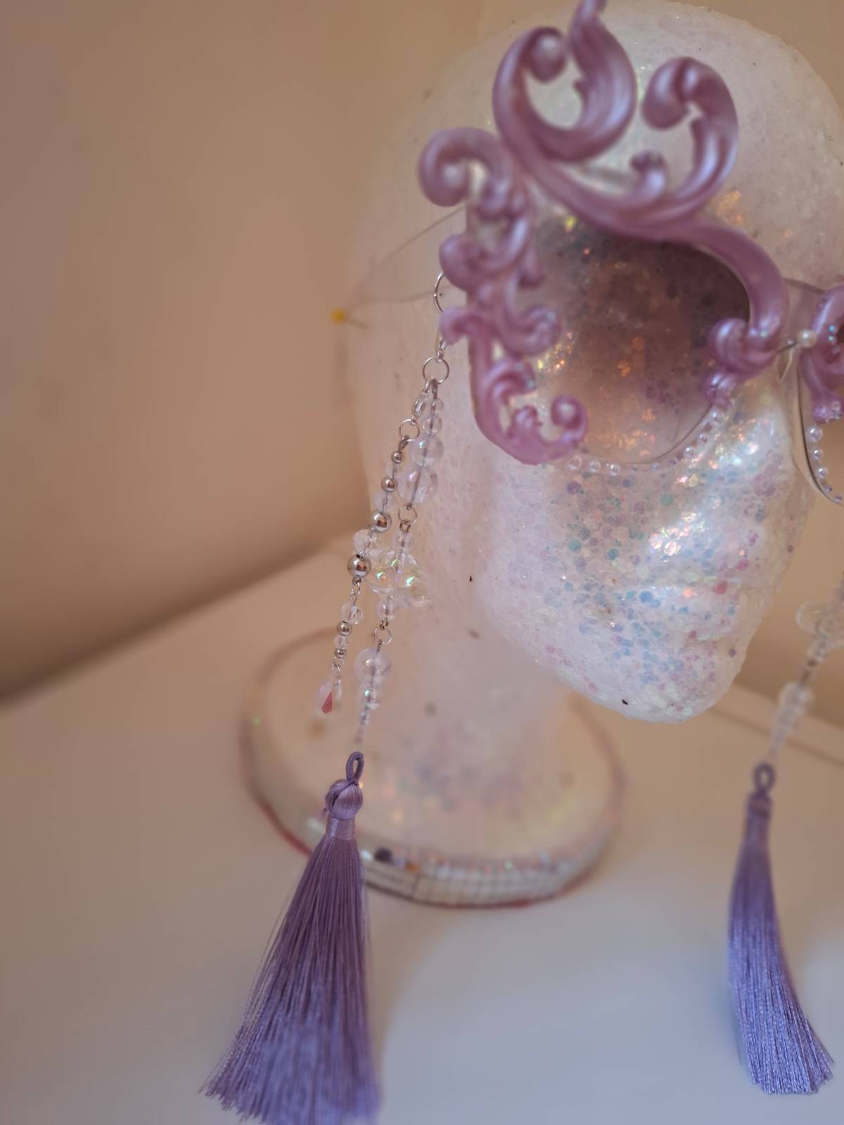 Hand-sculpted sunglasses in soft lavender scrollwork with opalescent pearls and lilac tassels.
